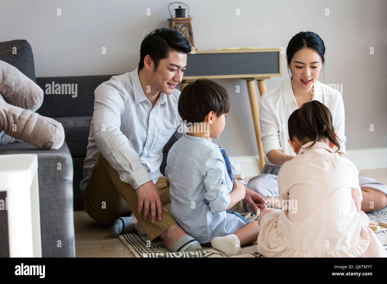 Un paio di genitori che accompagnano i loro due figli e figlie giocando con blocchi sul tappeto del soggiorno - foto di scorta Foto Stock