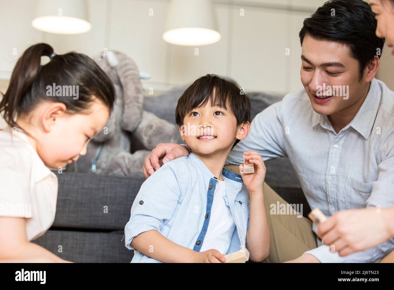 Un paio di genitori che accompagnano i loro due figli e figlie giocando con blocchi sul tappeto del soggiorno - foto di scorta Foto Stock