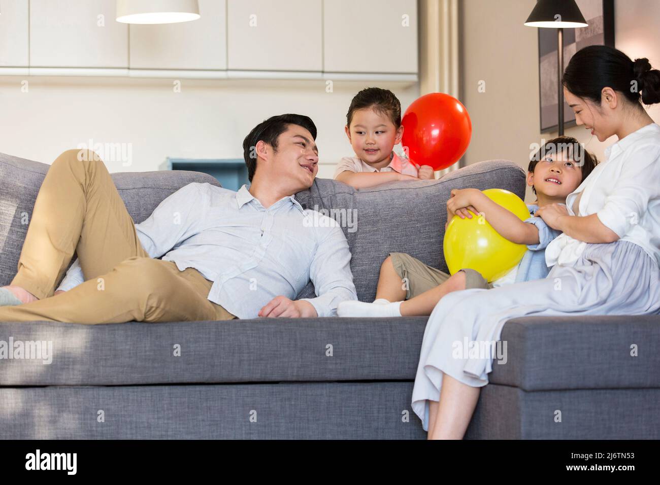 Una giovane famiglia di quattro persone che si inzellano sul divano godendo il loro tempo di vacanza - foto di scorta Foto Stock