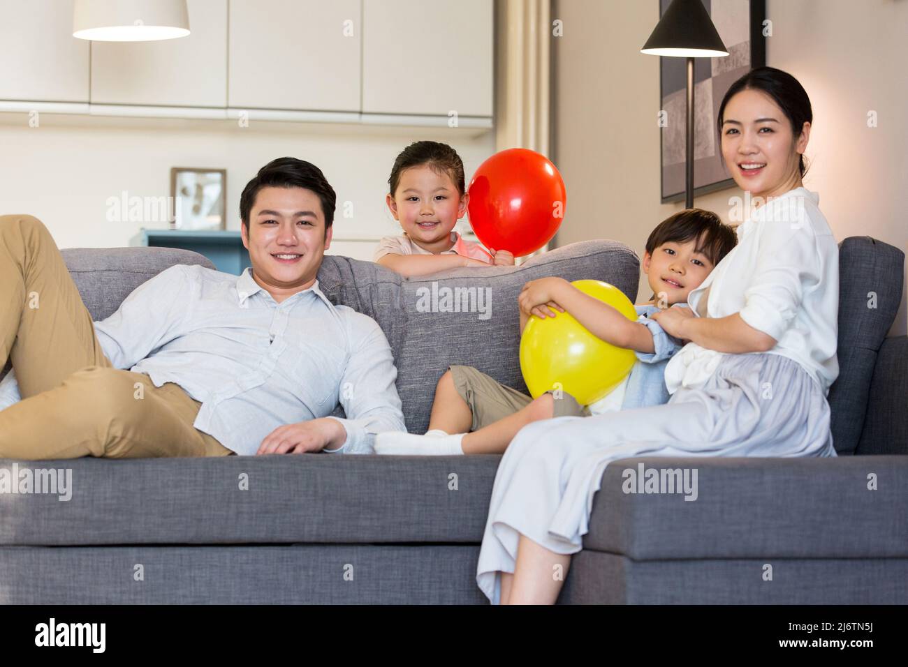Una giovane famiglia di quattro persone che si inzellano sul divano godendo il loro tempo di vacanza - foto di scorta Foto Stock