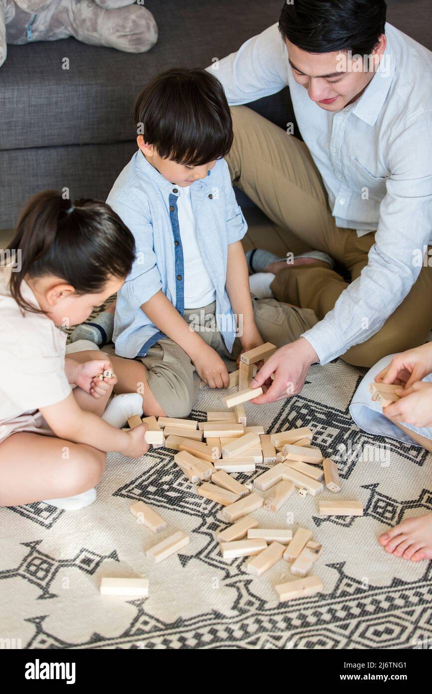 Un paio di genitori che accompagnano i loro due figli e figlie giocando con blocchi sul tappeto del soggiorno - foto di scorta Foto Stock