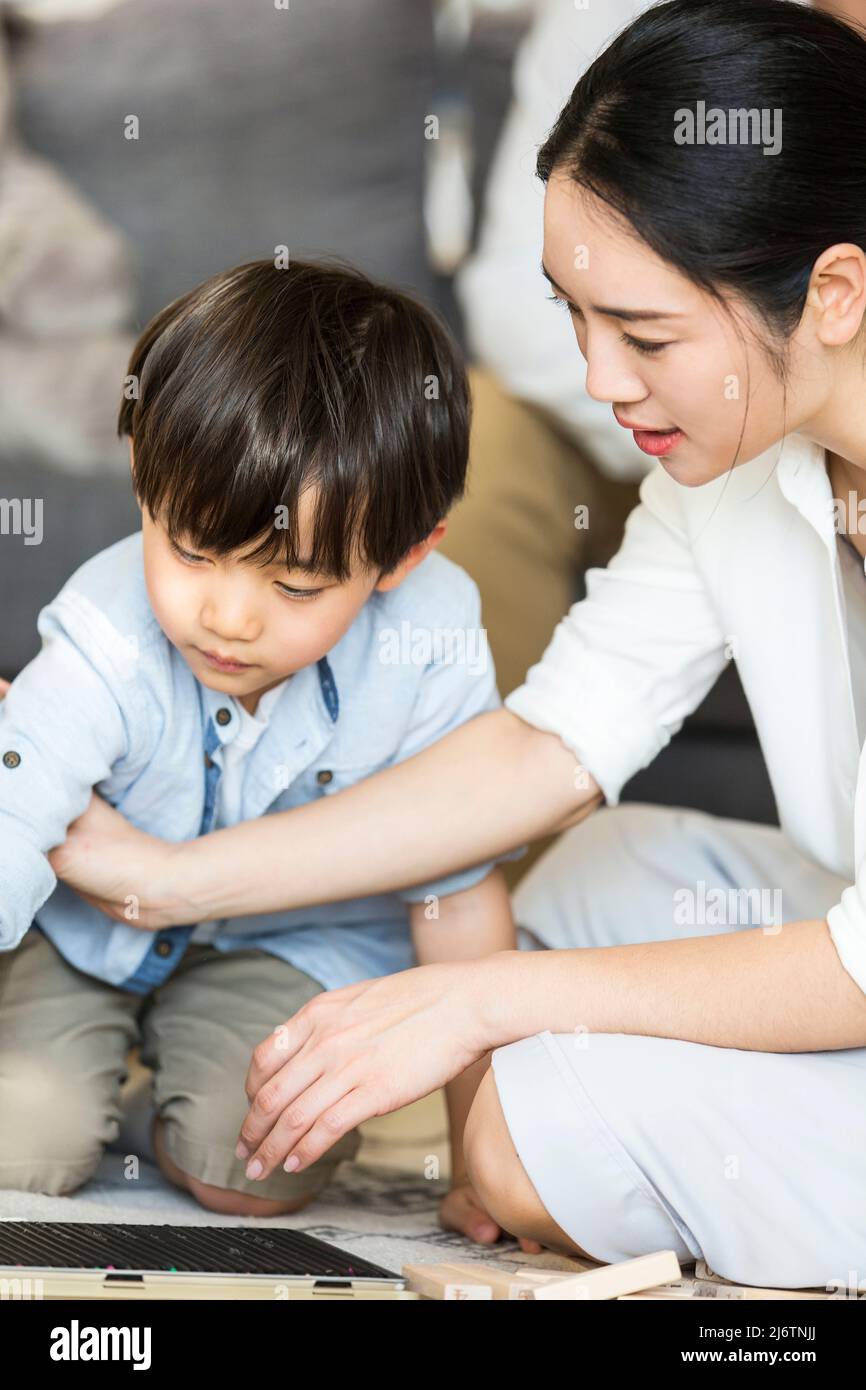 Una giovane madre è seduta sul tappeto pazientemente accompagnando il suo bambino per disegnare disegni a matita - foto di scorta Foto Stock