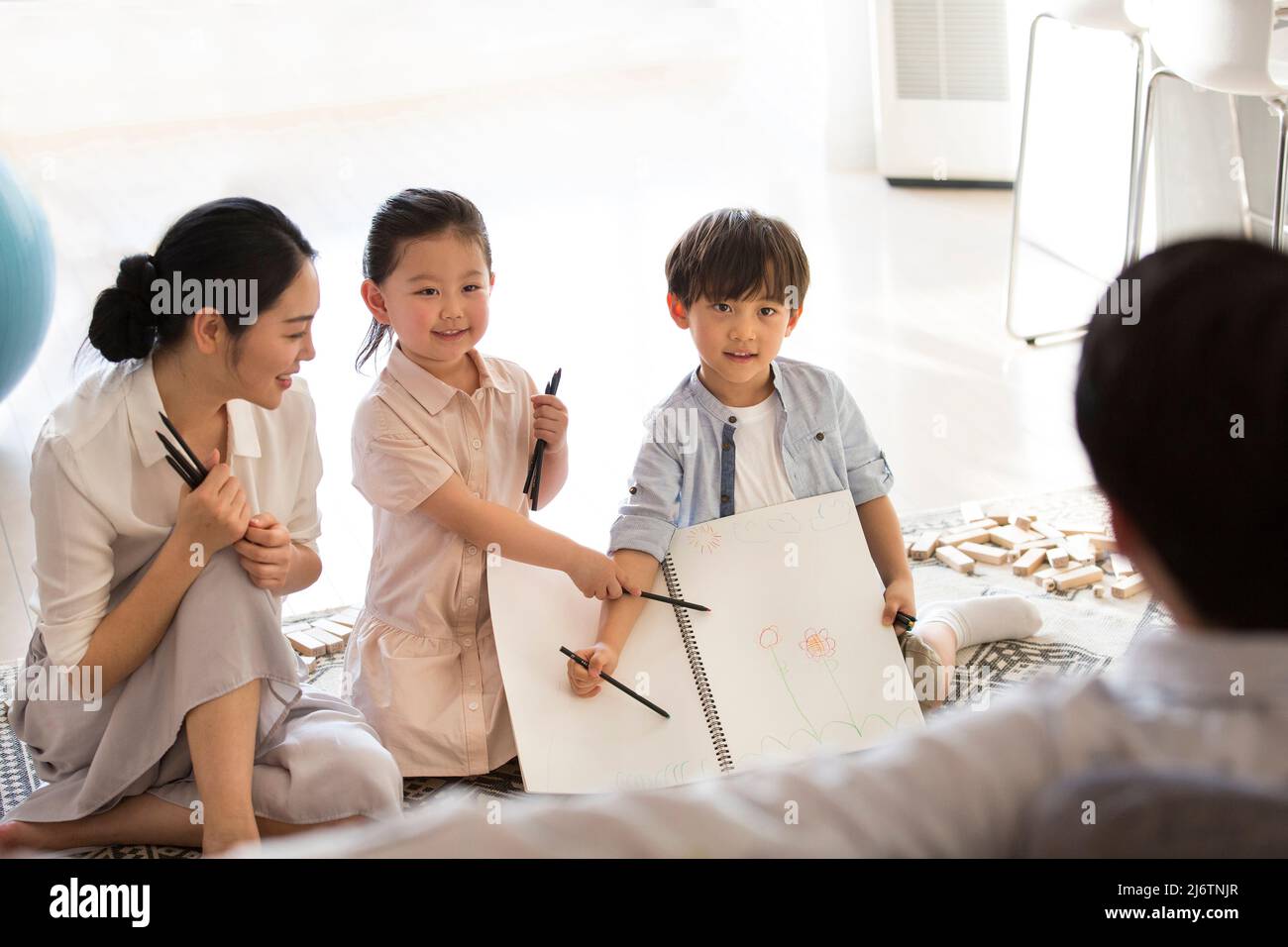 Un ragazzo e una ragazza raccontano al padre i disegni dei loro figli, mentre la madre guarda in delizia - foto di scorta Foto Stock
