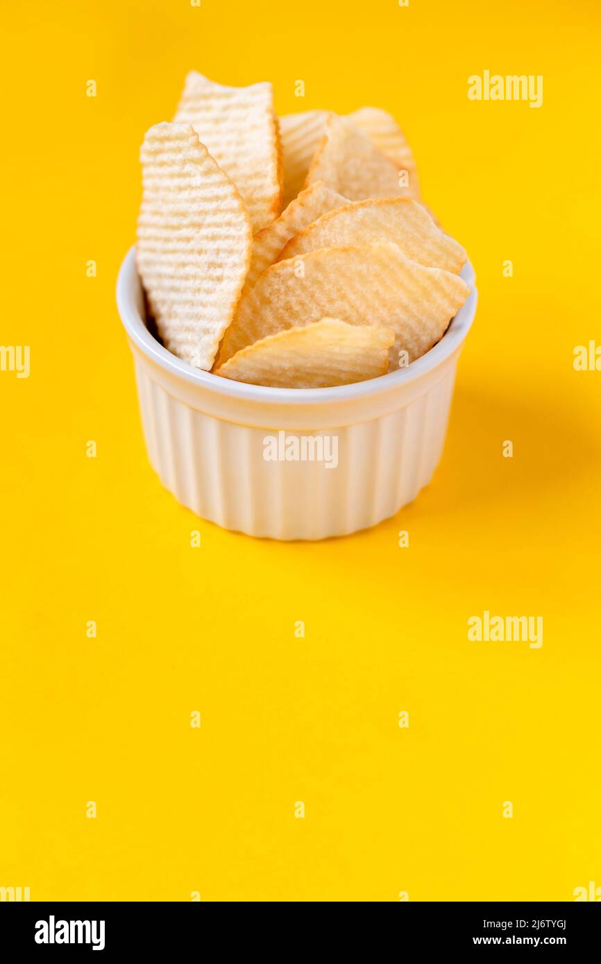Patatine fritte in ceramica bianca su sfondo giallo. Cibo malsano spazzatura, patatine, cibo da festa, concetto di fast food, spazio libero per il testo Foto Stock