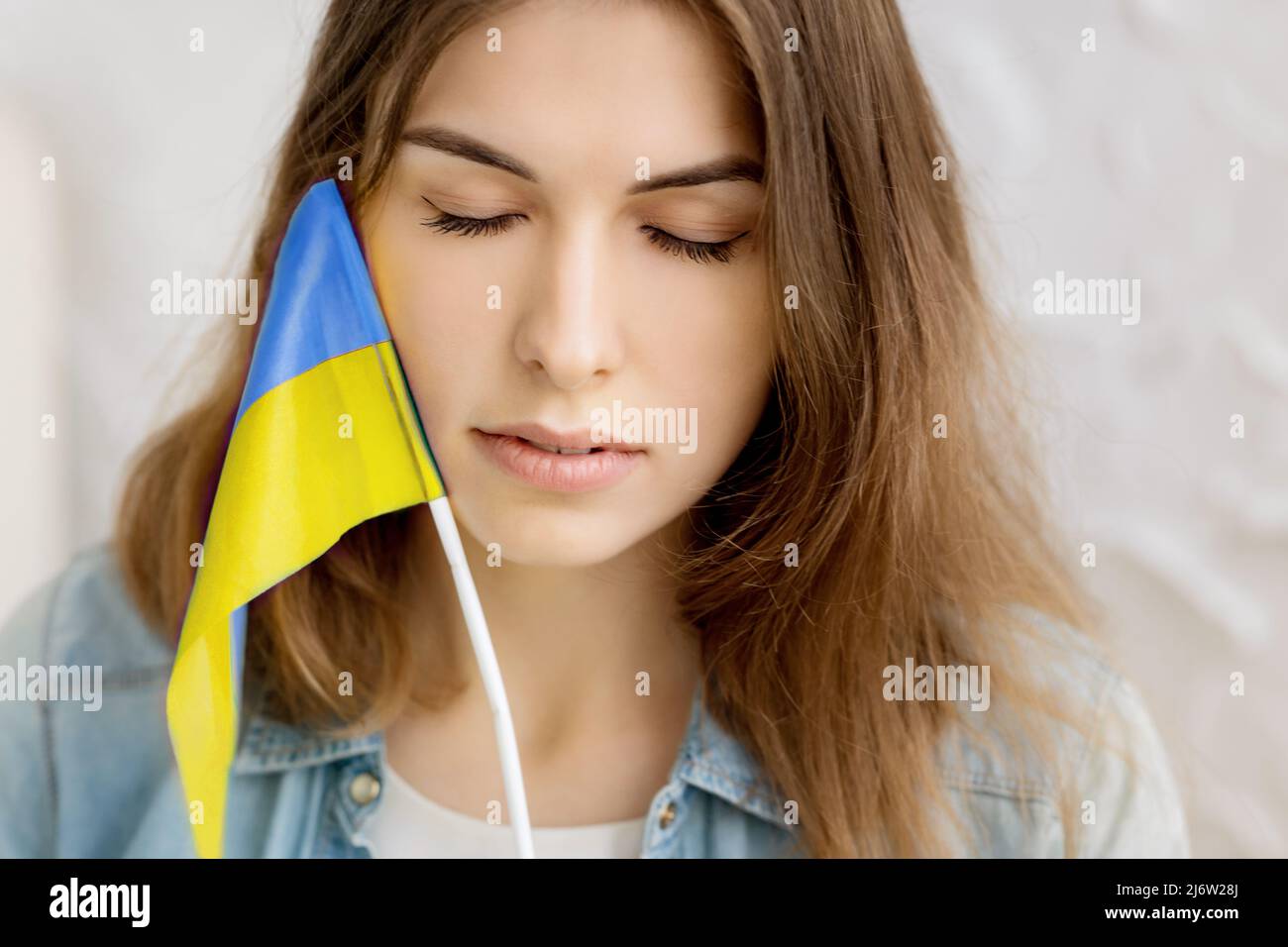 La ragazza seria indipendente tiene la bandiera Ucraina e gli occhi vicini. Patriot del suo paese. Prega per l'Ucraina. Lotta per la libertà. Stop guerra. Blu giallo. Foto Stock