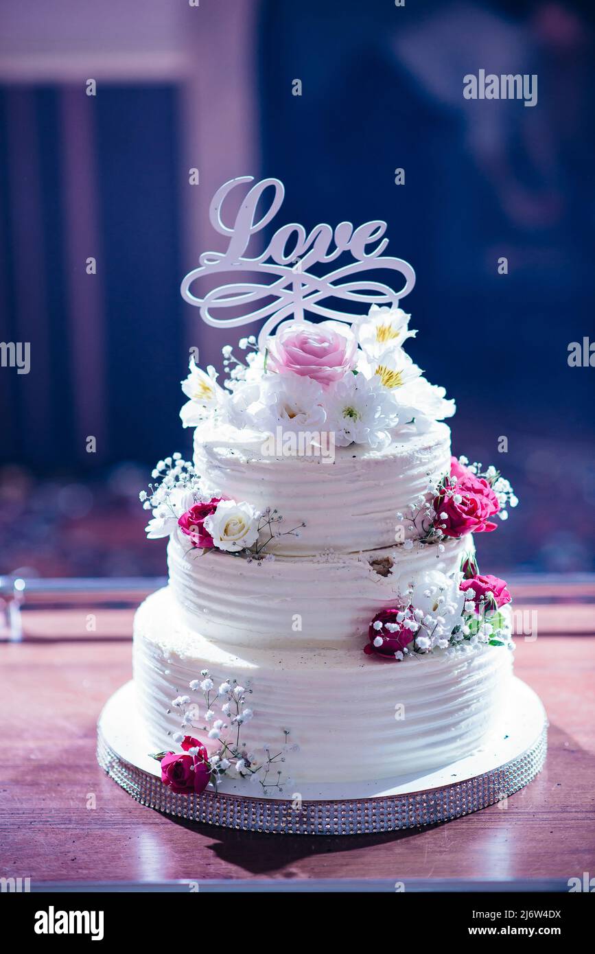 Elegante torta nuziale su tre piani con decorazione commestibile a forma di  rose, nastri e cuore in ambiente naturale, illuminata dal sole Foto stock -  Alamy