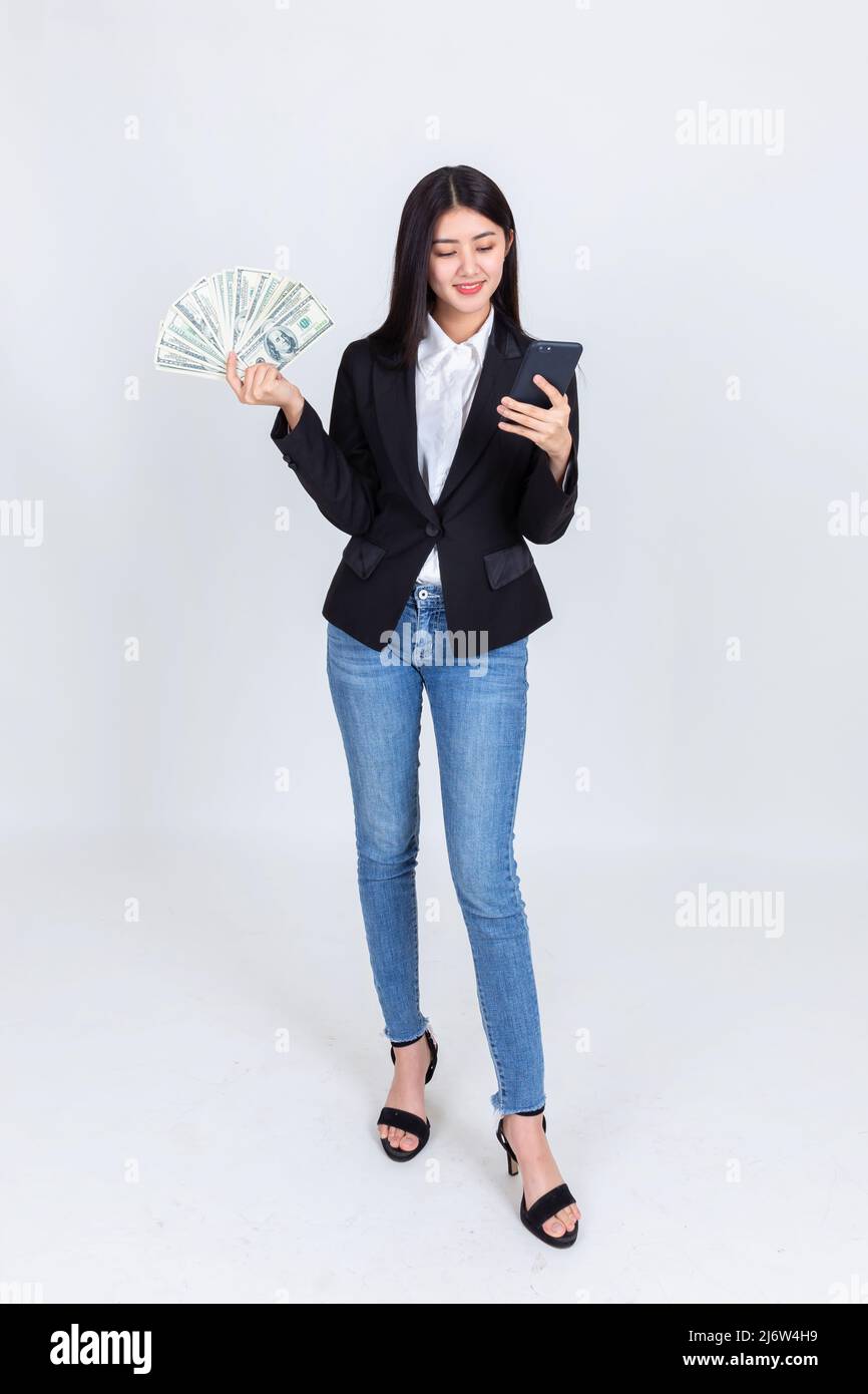 Affari asian donna che indossa abbigliamento da ufficio di successo tenere smartphone cellulare e US dollari in mano sensazione di felice e sorriso, fallimento econo Foto Stock