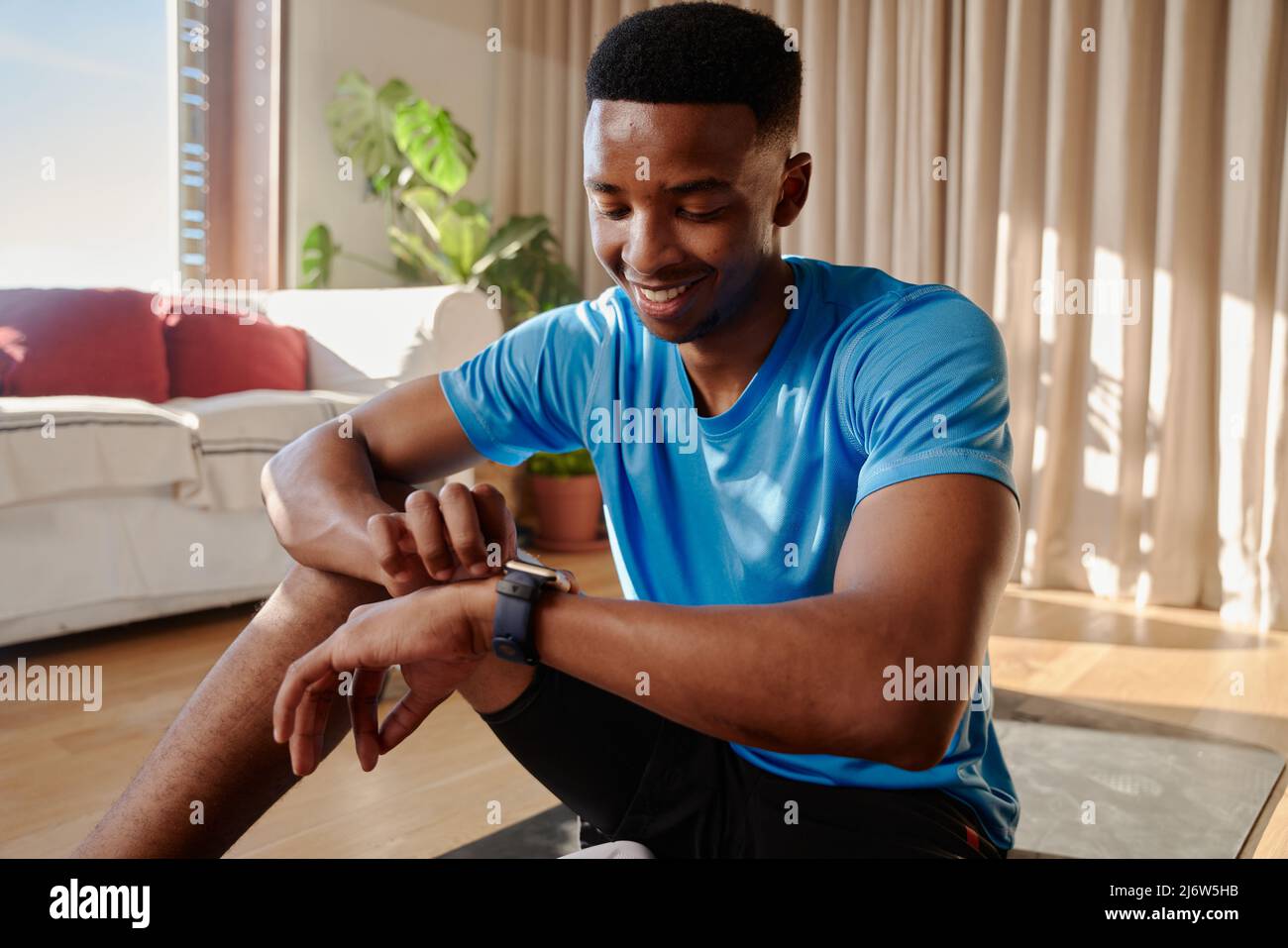 Giovane allegro africano americano nero maschio che si allenano a casa su tappeto yoga controllo smart watch. Mantenere la sua forma fisica Foto Stock