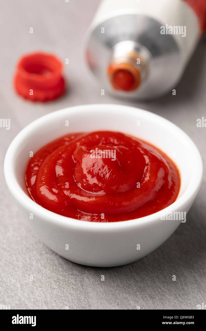 Ciotola con il ketchup di pomodoro da vicino e un tubetto di ketchup di pomodoro sullo sfondo Foto Stock