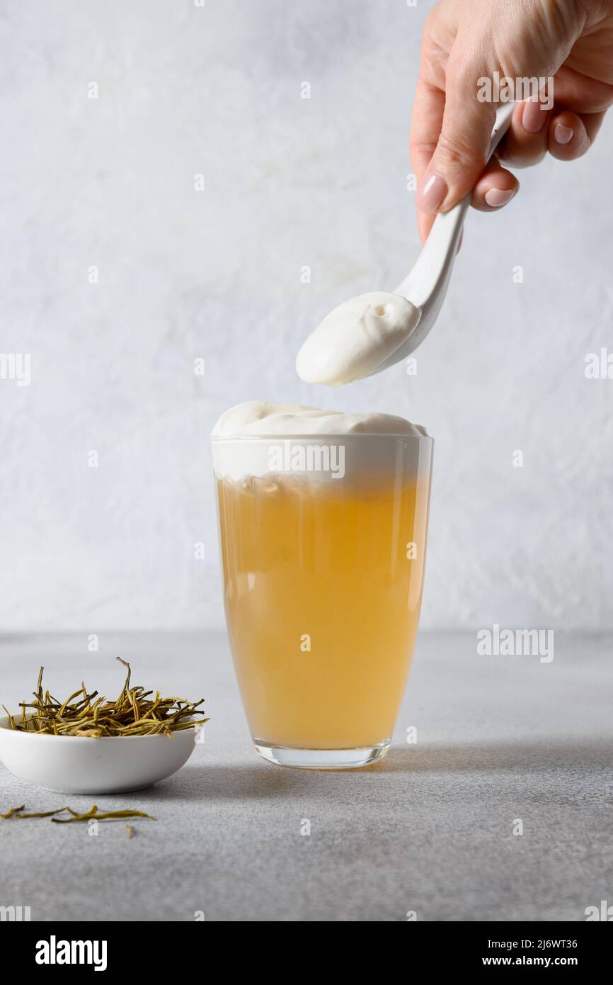 Tè al formaggio cinese con bevande asiatiche in vetro con strato di schiuma di formaggio panna montata su sfondo bianco. Formato verticale. Donna che cucinano il tè. Foto Stock