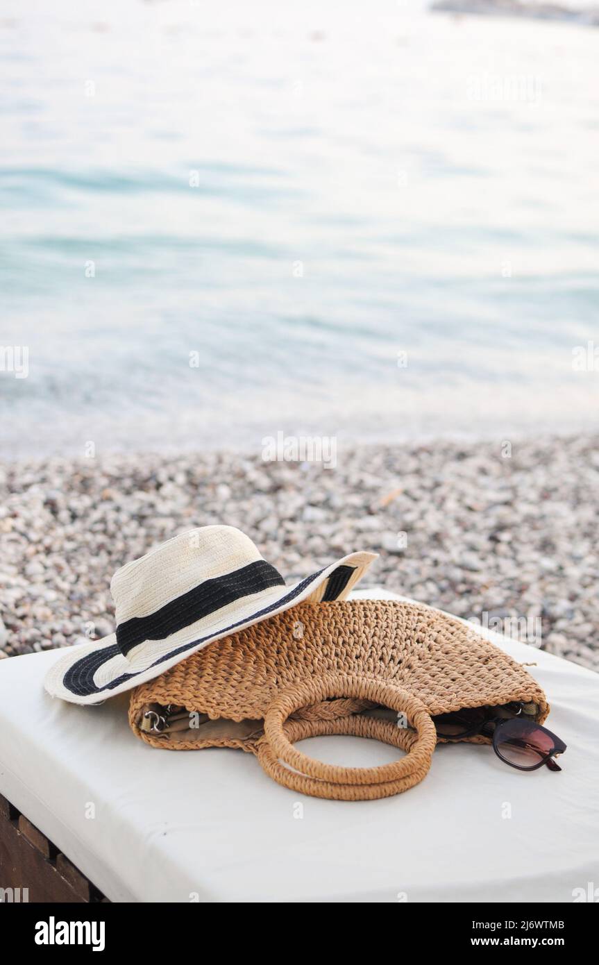 Accessori da spiaggia: Cappello di paglia, borsa a maglia estiva e occhiali  da sole sul lettino vicino al mare sulla spiaggia di ciottoli Foto stock -  Alamy