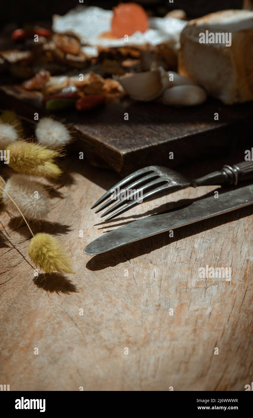 Vecchio coltello in metallo vintage con forchetta e coda di coniglio secchi fiori di erba su vecchio rustico tavolo da pranzo in legno. Concetto di mangiare, spazio di copia, fuoco selettivo. Foto Stock