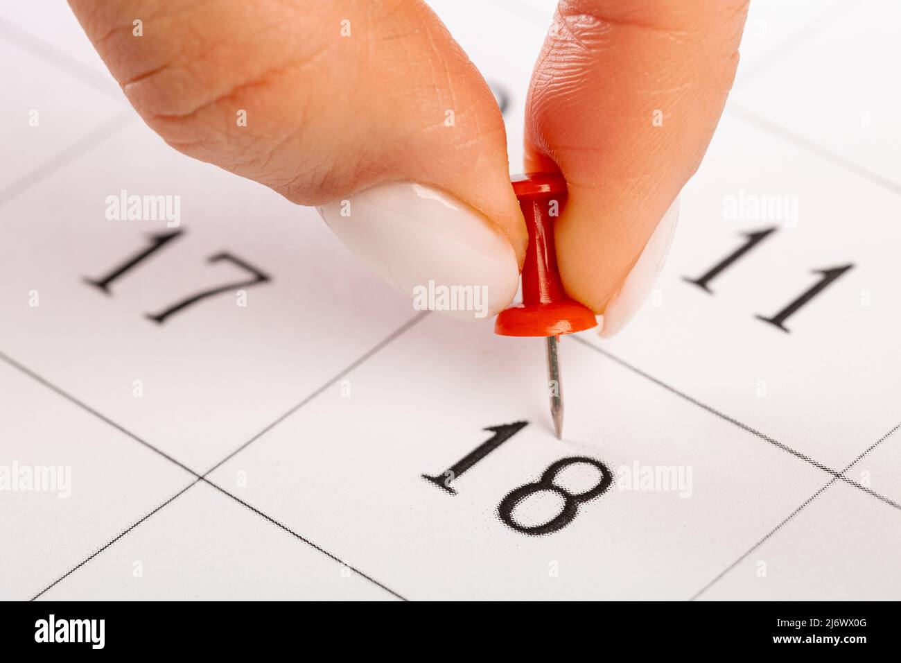 Pin a mano rosso bloccato il giorno del mese nel calendario, business concept. Belle dita a mano femminile Foto Stock