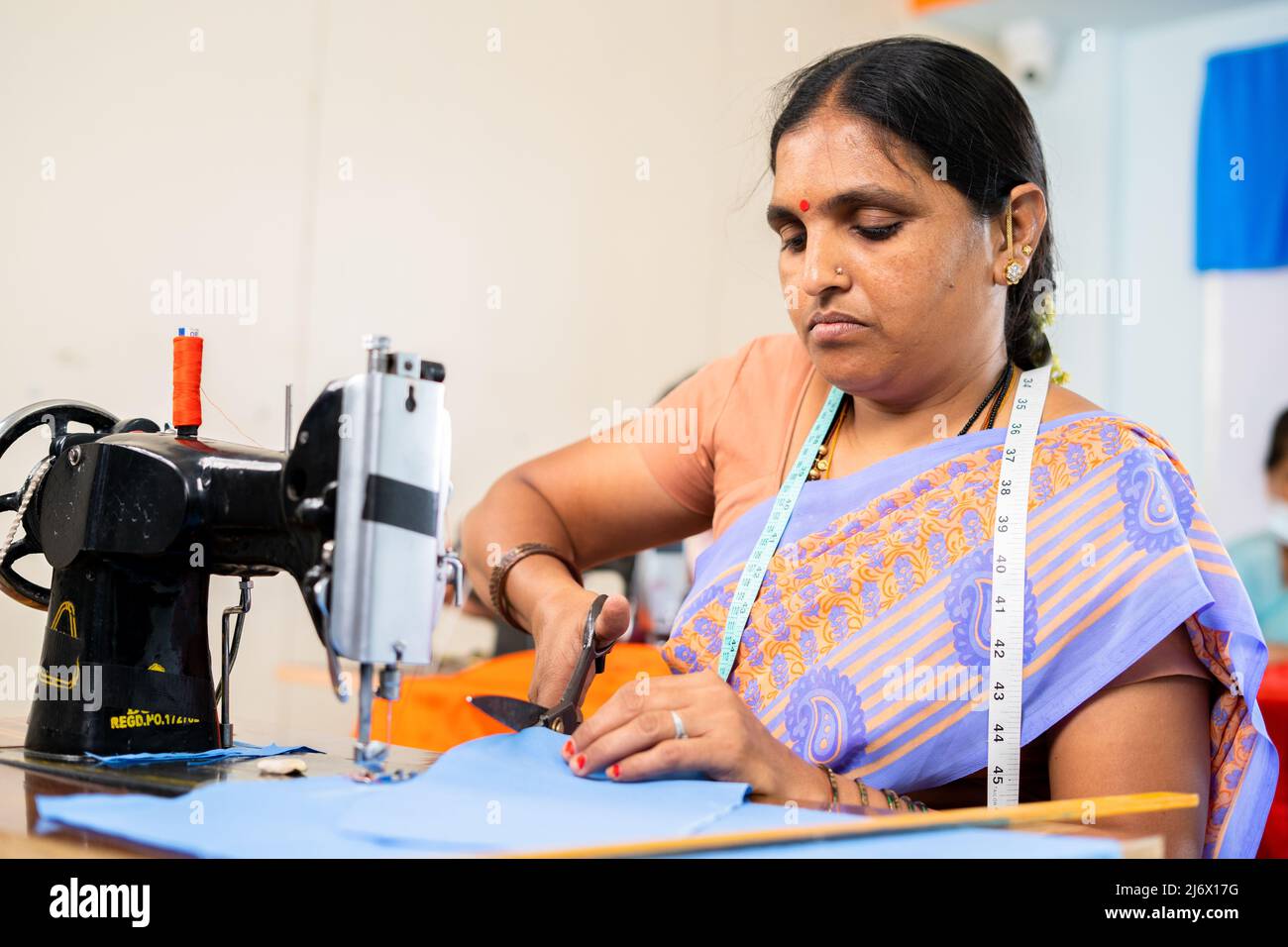 Donna indiana a capi di lavoro occupato tagliando vestiti vicino segatrice macchina - concetto di empowerment, competenza e piccola impresa Foto Stock