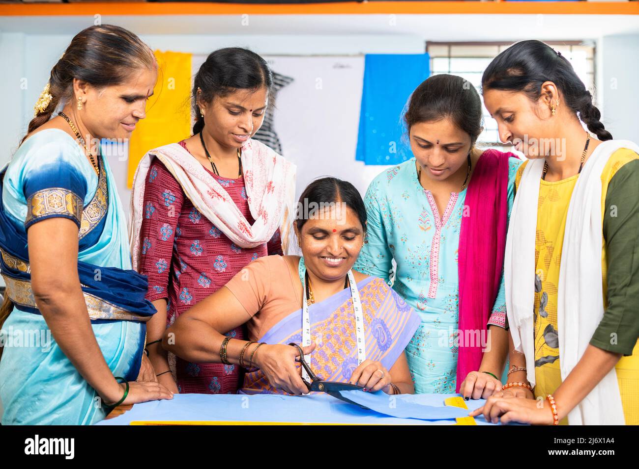 il formatore spiega o guida per tagliare i vestiti a gruppo di donne studenti al centro di formazione - concetto di apprendimento, empowerment e occupazione Foto Stock