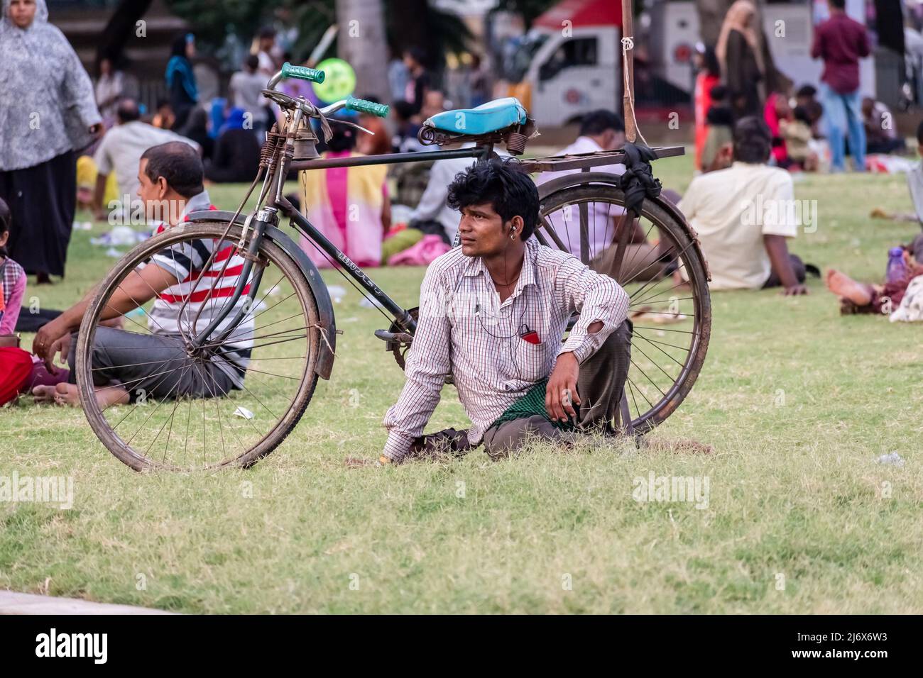 Vellore, Tamil Nadu, India - Settembre 2018: Un ritratto candido di un uomo indiano seduto da solo su erba verde accanto alla sua bicicletta in un parco pubblico. Foto Stock