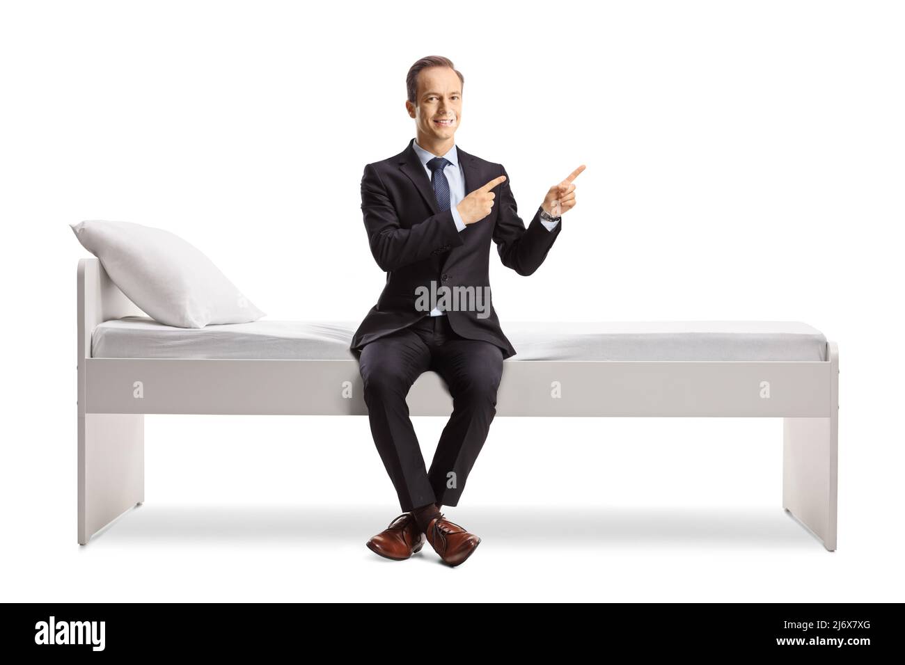 Uomo d'affari seduto su un letto e puntando con entrambe le dita verso il lato isolato su sfondo bianco Foto Stock