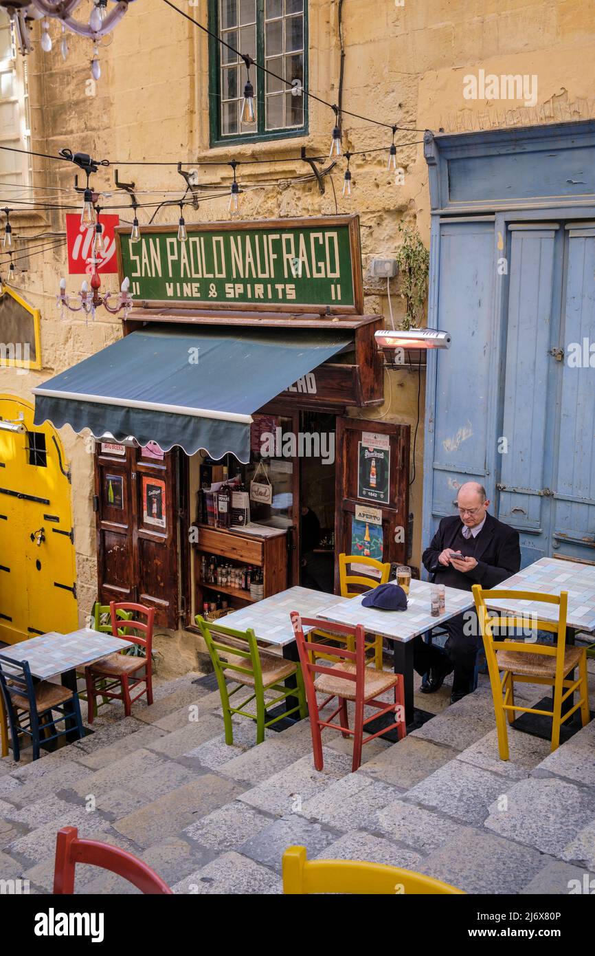 Un uomo che gode di un drink tranquillo in una strada laterale di Valletta, Malta Foto Stock