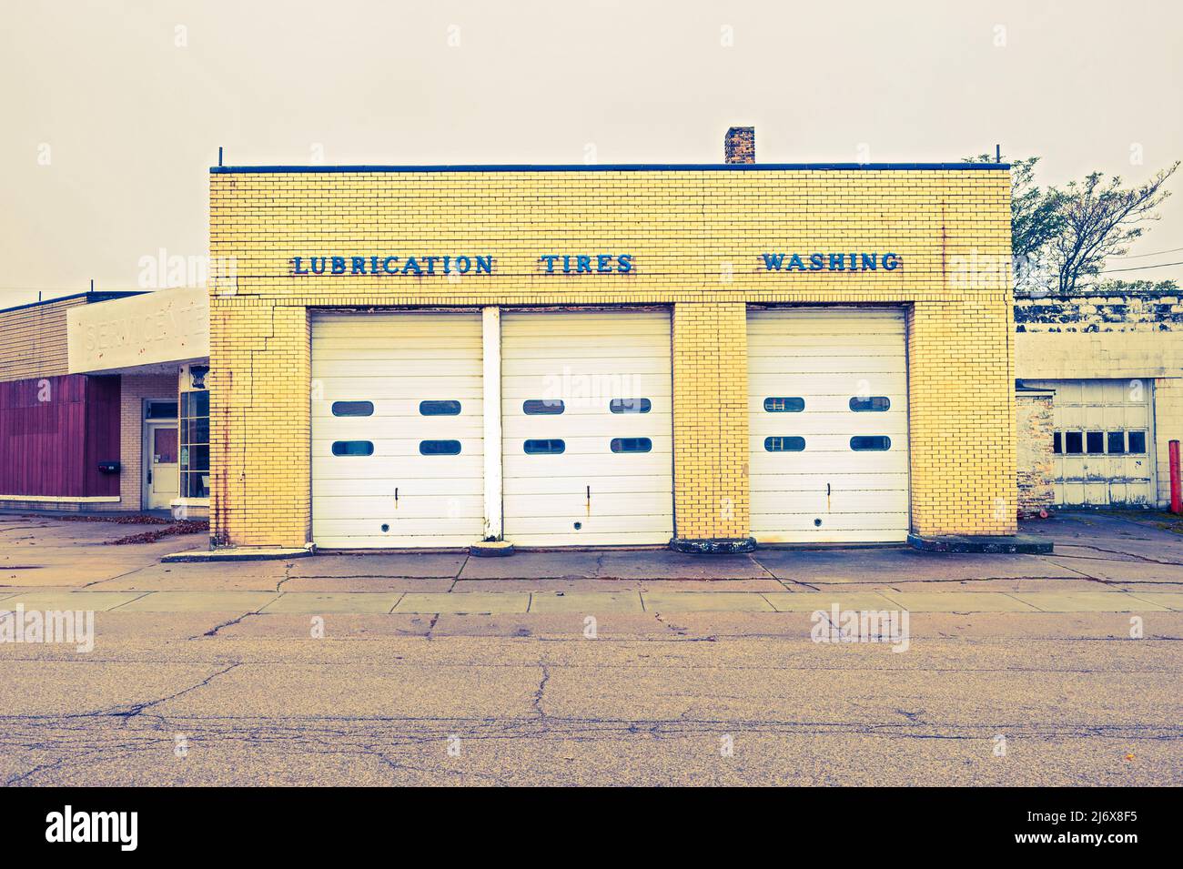 Negozio di riparazione di automobili di design classico, ora demolito, con segnaletica sopra le porte del garage, 'Lubration', 'Tires', 'lavatrice' a Ludington, Michigan, U Foto Stock