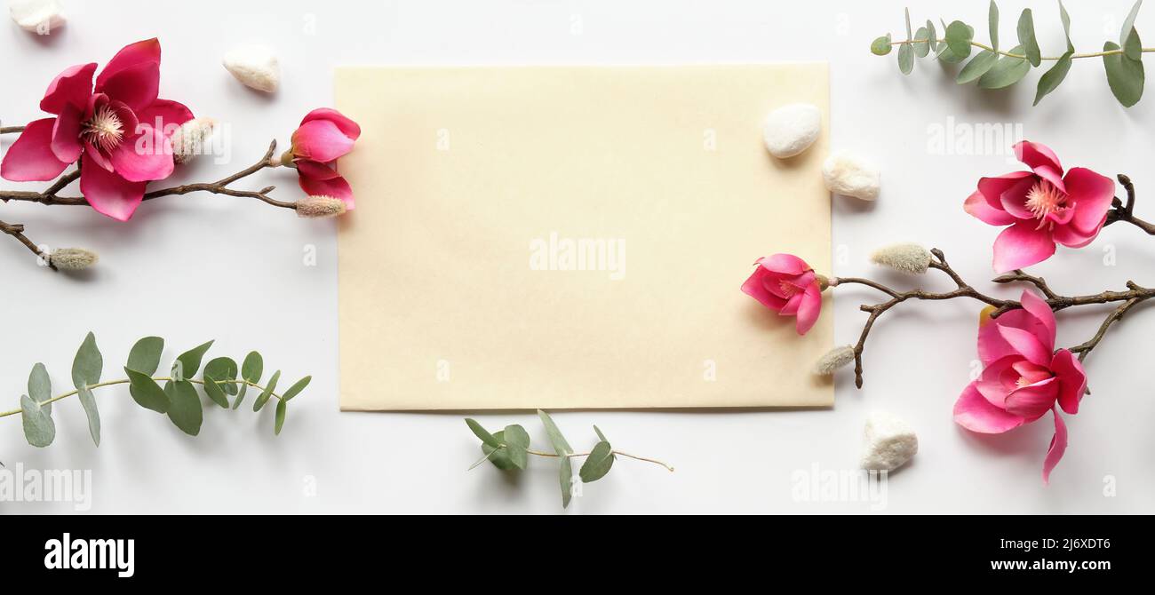 rosa magnolia fiori su rametti, foglie di eucalipto fresco. Cartoncino rosa vuoto con busta grigia. Foto Stock