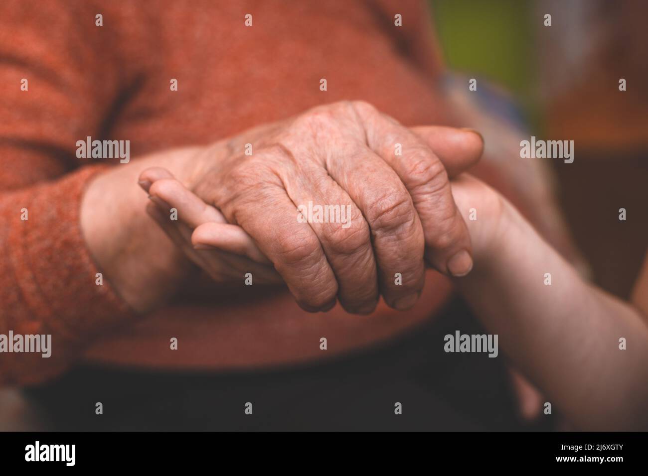 Le mani del nipote tengono la mano rugosa di una nonna anziana malata a casa. Il concetto di amore e cura. Movimento lento. Foto Stock