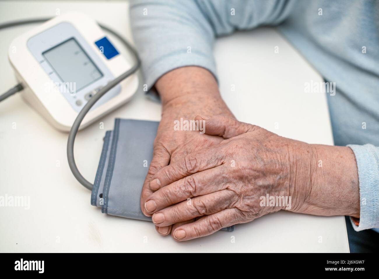 Le mani di una nonna matura di 93 anni con rughe sono a casa su un dispositivo di misurazione della pressione - un tonometro in una clinica medica. Il concetto Foto Stock