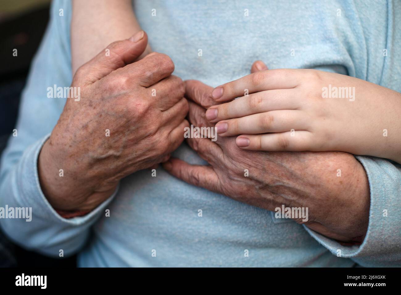 Le mani spiegazzate di una vecchia nonna tengono le mani di un nipote che la abbraccia. Il concetto di amore e cura. Vita lenta. Foto Stock