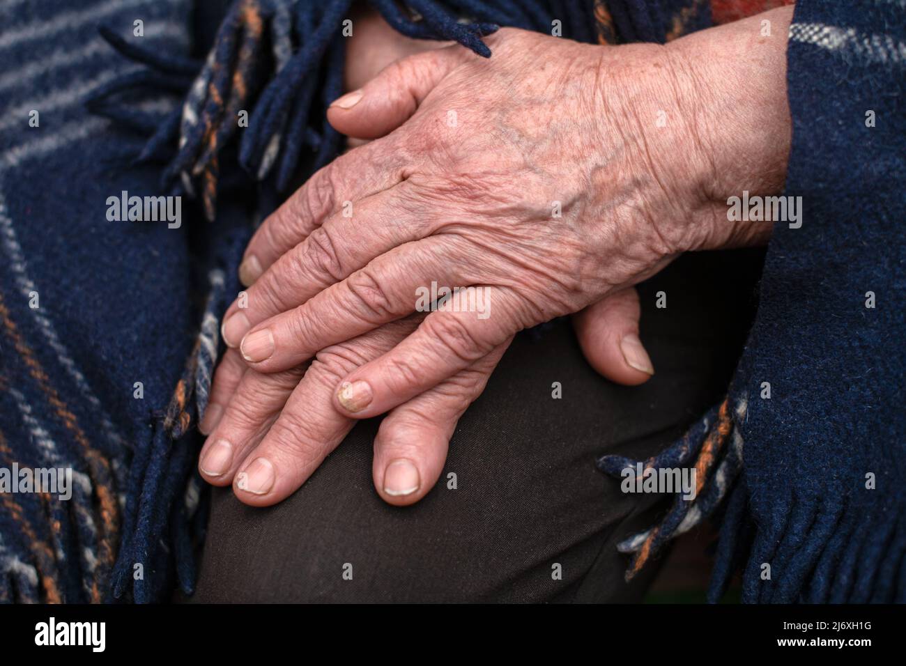 Le mani di una nonna matura di 93 anni con rughe giacciono su una coperta accogliente a casa. Il concetto di amore e cura. Movimento lento. Foto Stock