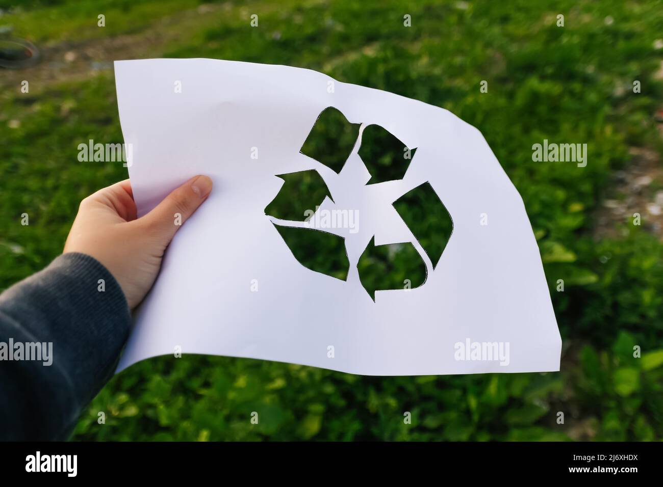 Defocus mano tenendo carta tagliata con il logo di verde erba natura spazzatura sfondo. Concetto di riciclaggio. Sfocato. Inquinamento del pianeta. Fuori fuoco Foto Stock