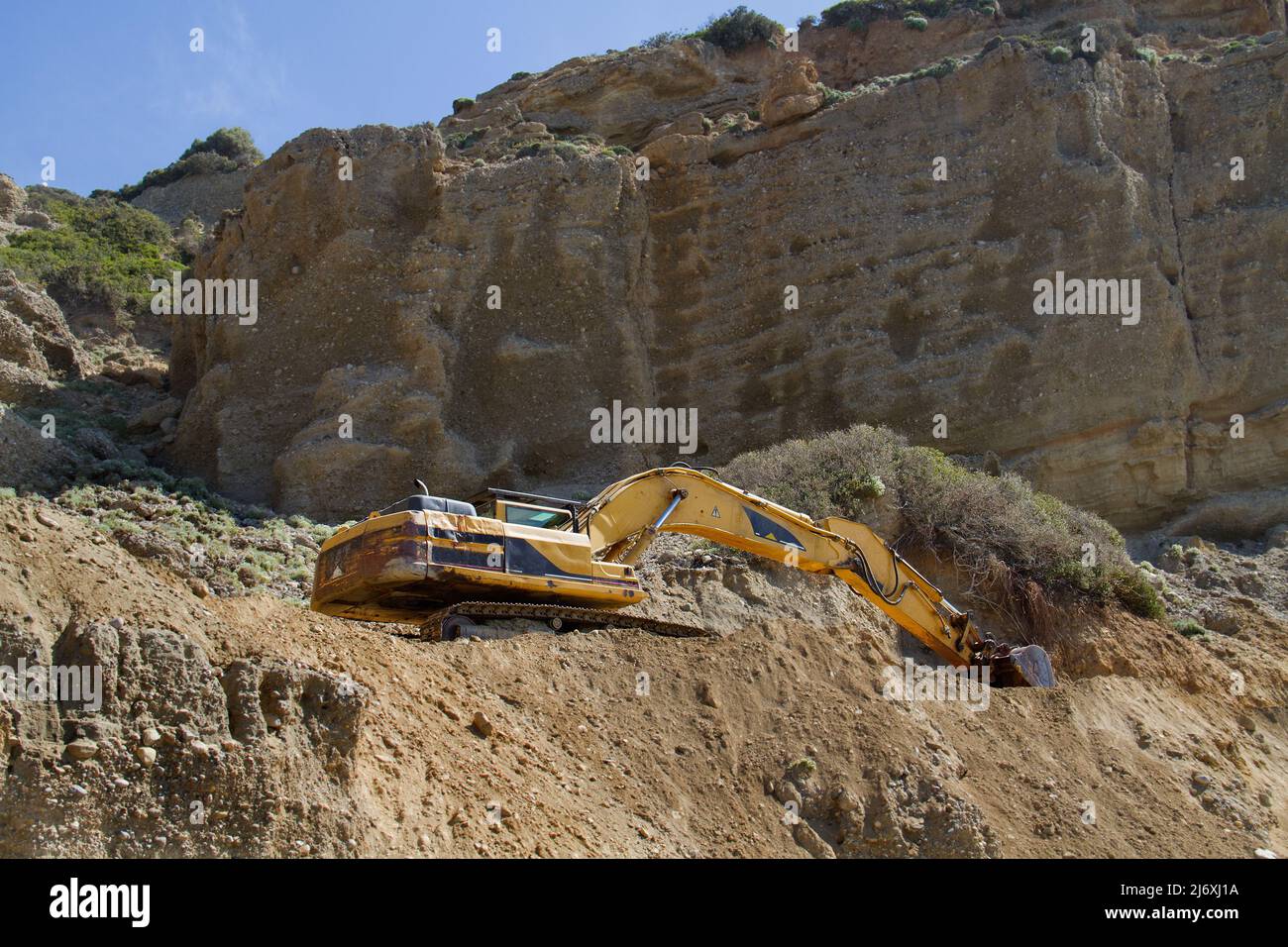 Escavatore cingolato giallo che lavora alla riparazione di una strada in montagna Foto Stock