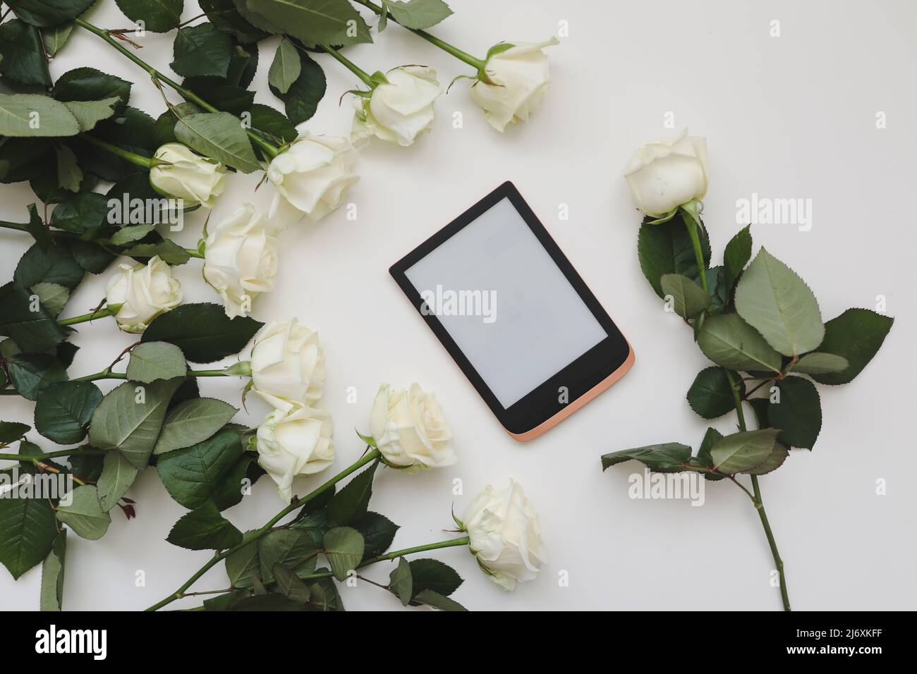 composizione floreale con tavoletta, rose fresche bianche su sfondo bianco. Scrivania da ufficio. Superficie piana, vista dall'alto. Copia modello spazio. Foto Stock