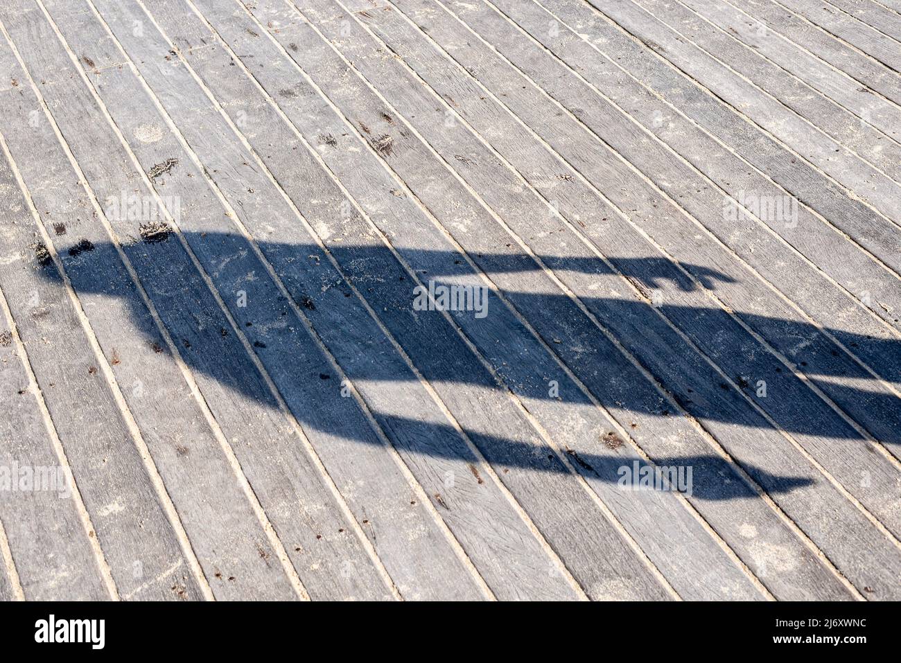 Ombra di una persona riflessa sul pavimento in legno di un molo. Salvador, Bahia, Brasile. Foto Stock