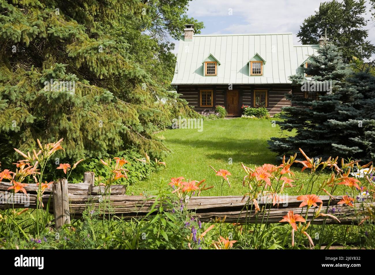 Vecchia casa di tronchi in stile Canadiana del 1800s con giardino paesaggistico protetto da recinzione rustica in legno. Foto Stock