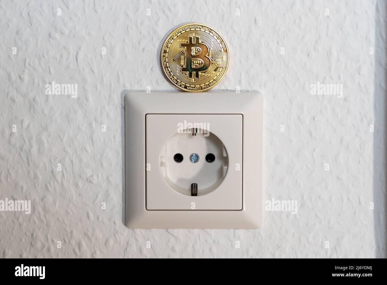 Bitcoin in piedi su una presa di alimentazione. Crypto Currency BTC che viene estratto con un elevato consumo energetico a causa della quantità di processi minerari. Foto Stock