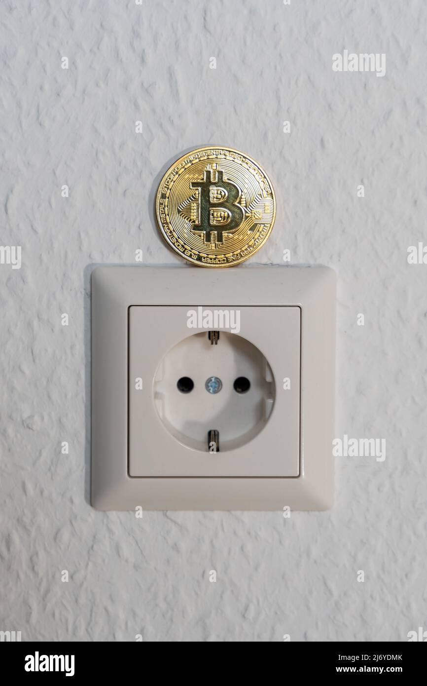 Bitcoin in piedi su una presa di alimentazione. Crypto Currency BTC che viene estratto con un elevato consumo energetico a causa della quantità di elaborazione GPU. Foto Stock