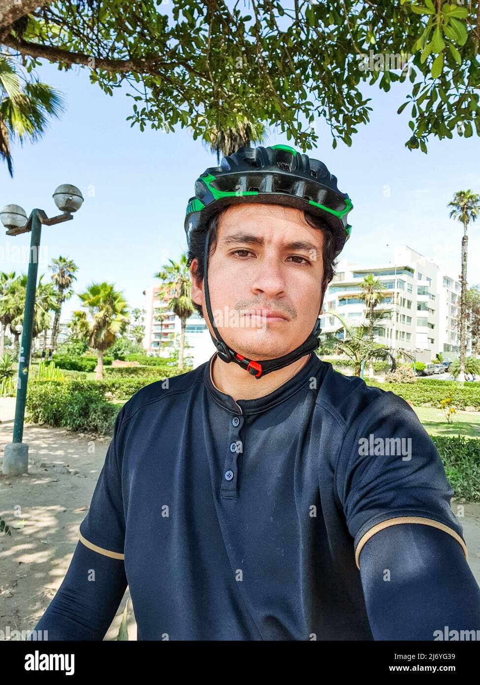 giovane e bello ciclista in abiti da ciclismo neri, indossando un casco in un parco Foto Stock