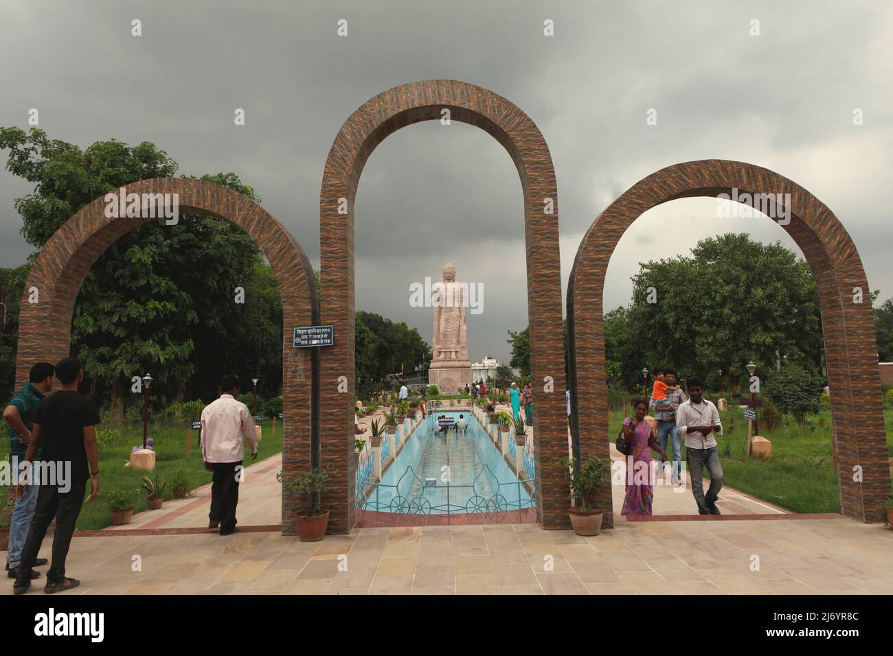 I visitatori alle porte curve che conducono a una statua in pietra arenaria alta 80 piedi del Buddha in piedi a Sarnath, alla periferia di Varanasi, Utar Pradesh, India. Costruita dal 1997 al 2011, la statua fu il risultato di uno sforzo congiunto tra Thailandia e India. Foto Stock