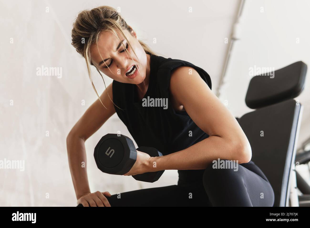 Donna atletica che fa esercizio di bicipite con manubri in palestra Foto Stock