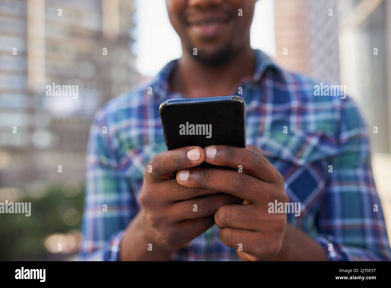 Un primo piano delle mani che testano sul cellulare con sfondo cittadino Foto Stock