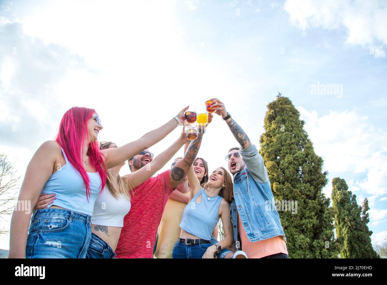 sette amici millenari che tostano a una festa all'aperto Foto Stock