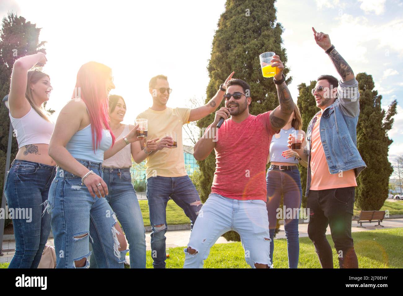 giovane che canta con il microfono con il suo gruppo di amiche per celebrare una festa all'aperto Foto Stock