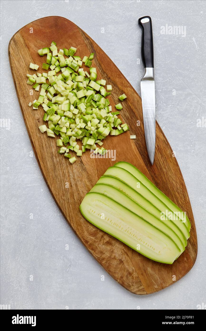 Zucchine tagliate a cubetti e a strati su un tagliere in legno su un tavolo in calcestruzzo leggero Foto Stock