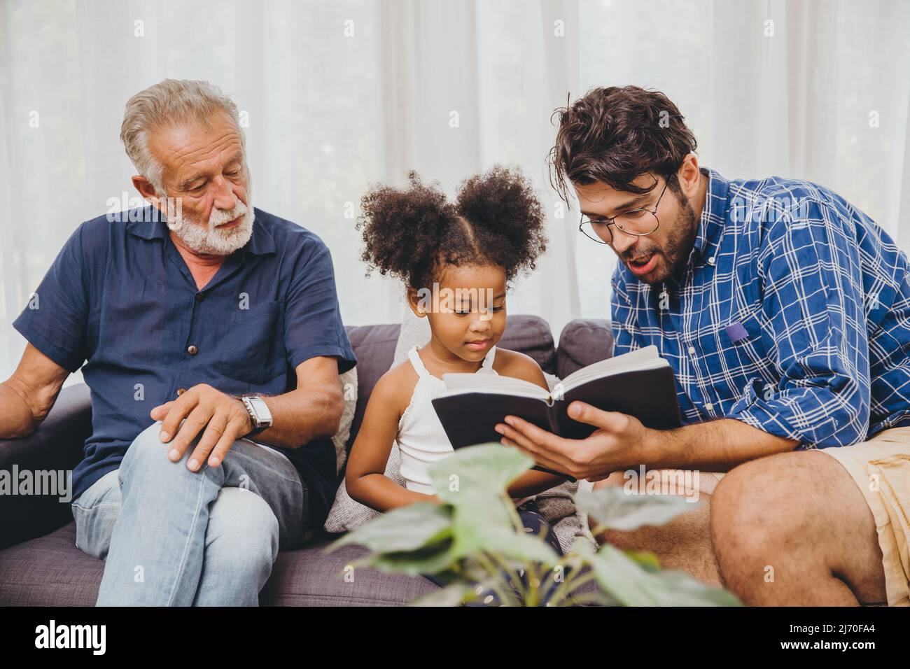Concetto di homeschooling. padre che insegna a bambino leggere un libro di autoeducazione nel soggiorno del divano di casa. Foto Stock