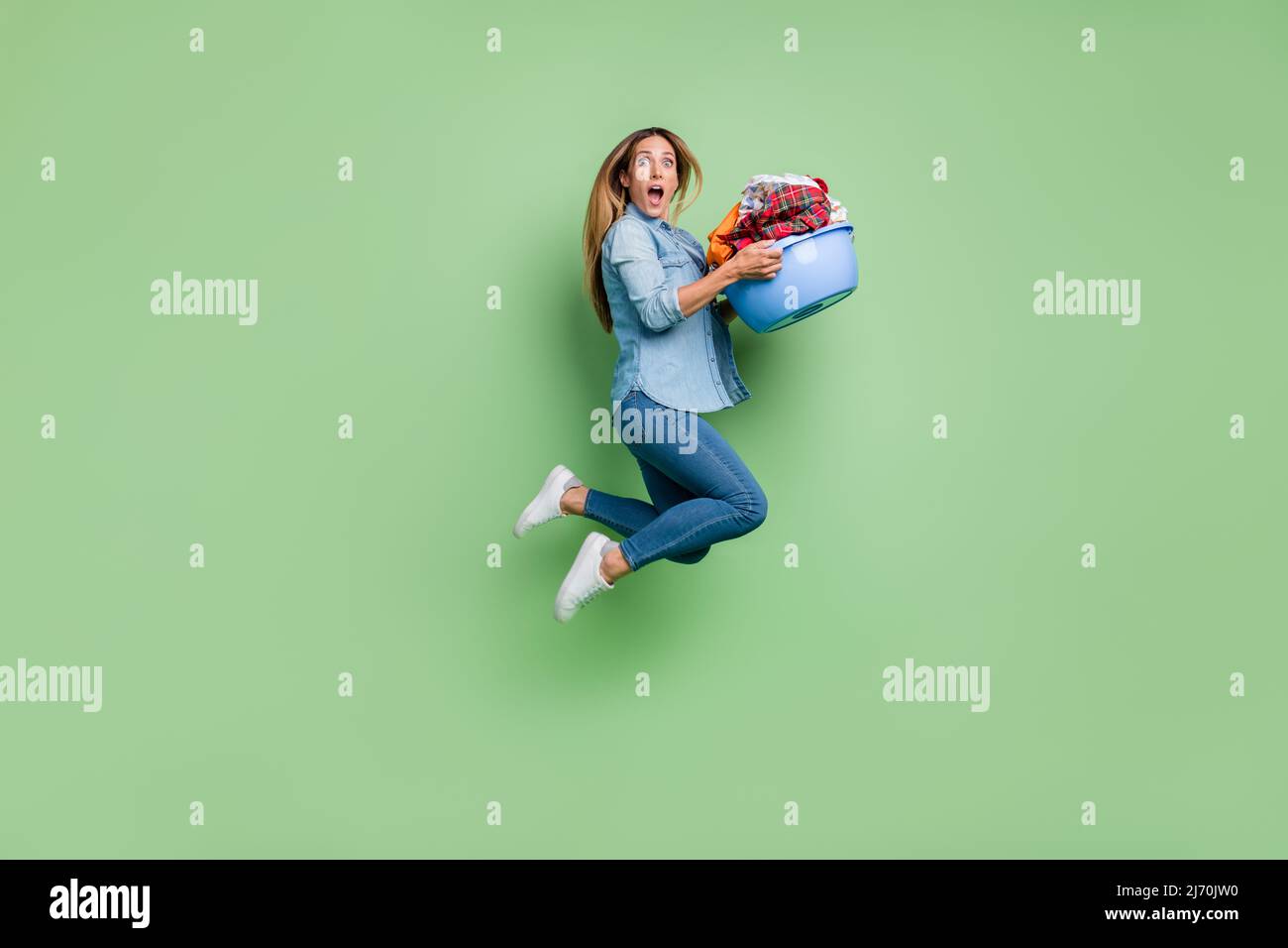 Foto di profilo a tutta lunghezza della giovane donna salto lavaggio stoffa indossare camicia jeans scarpe isolato su sfondo verde Foto Stock