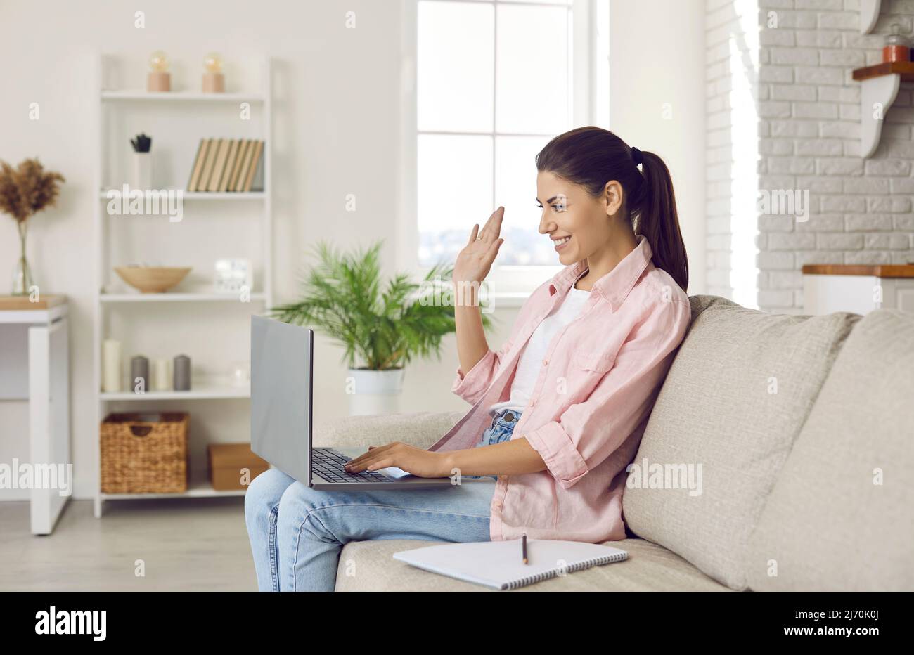 Donna che si sta muovendo di fronte alla webcam del portatile, accogliendo i partecipanti alla conferenza durante la riunione online. Foto Stock