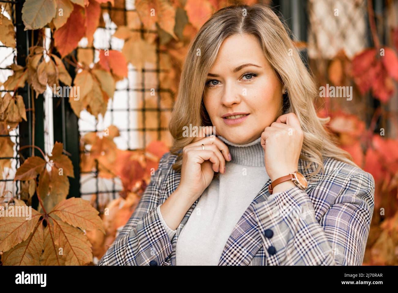 Donna d'affari vicino alle piante rampicanti su recinto con foglie rosse e gialle in autunno parco della città closeup. Donna adulta a piedi e rilassarsi sulla strada, la natura Foto Stock