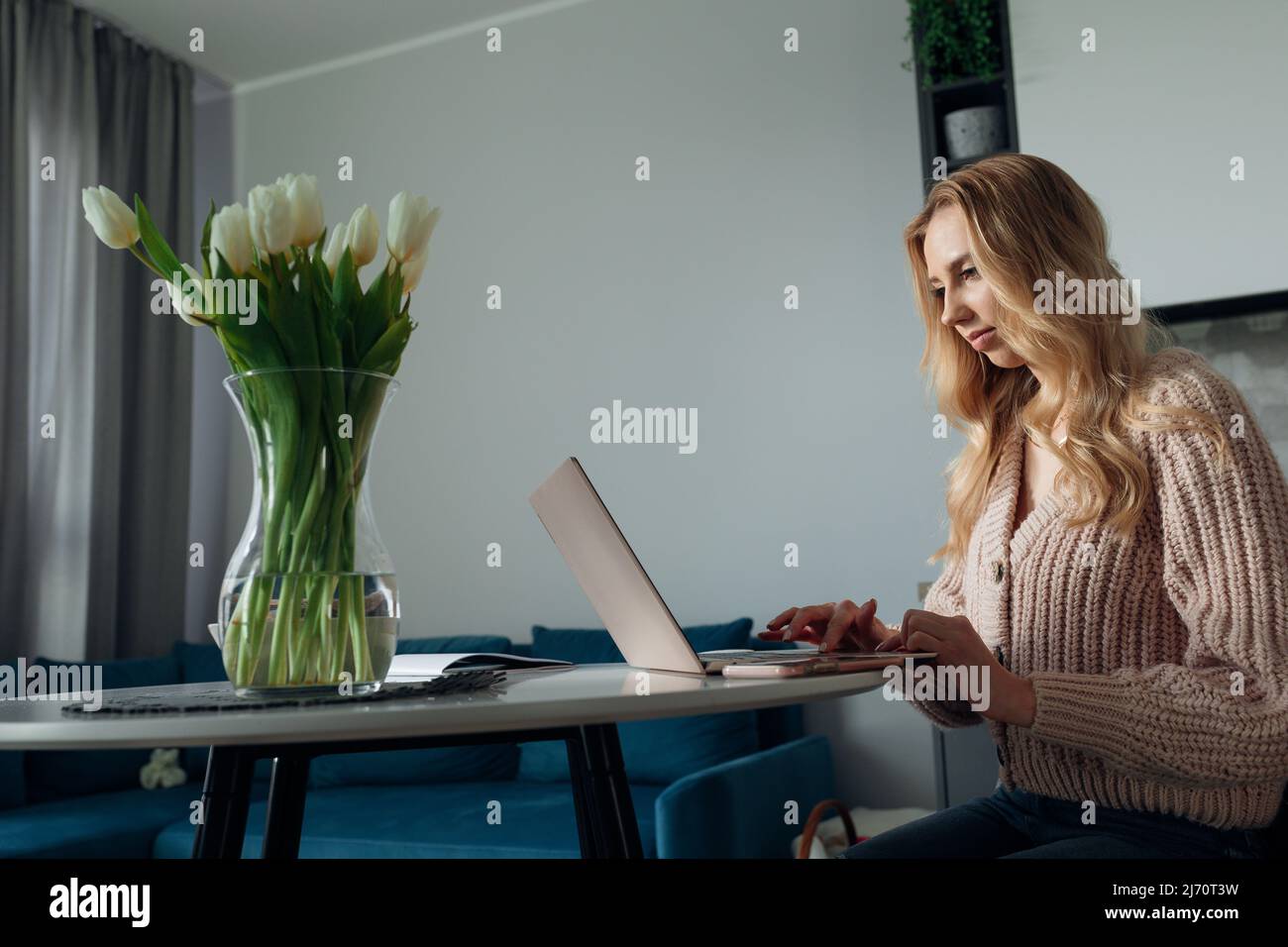 Giovane donna impegnata seduta sul posto di lavoro di mattina e lavoro sulla vista laterale del laptop. Ritratto di signora in abiti casual liberelancing da casa. Concetto di Foto Stock