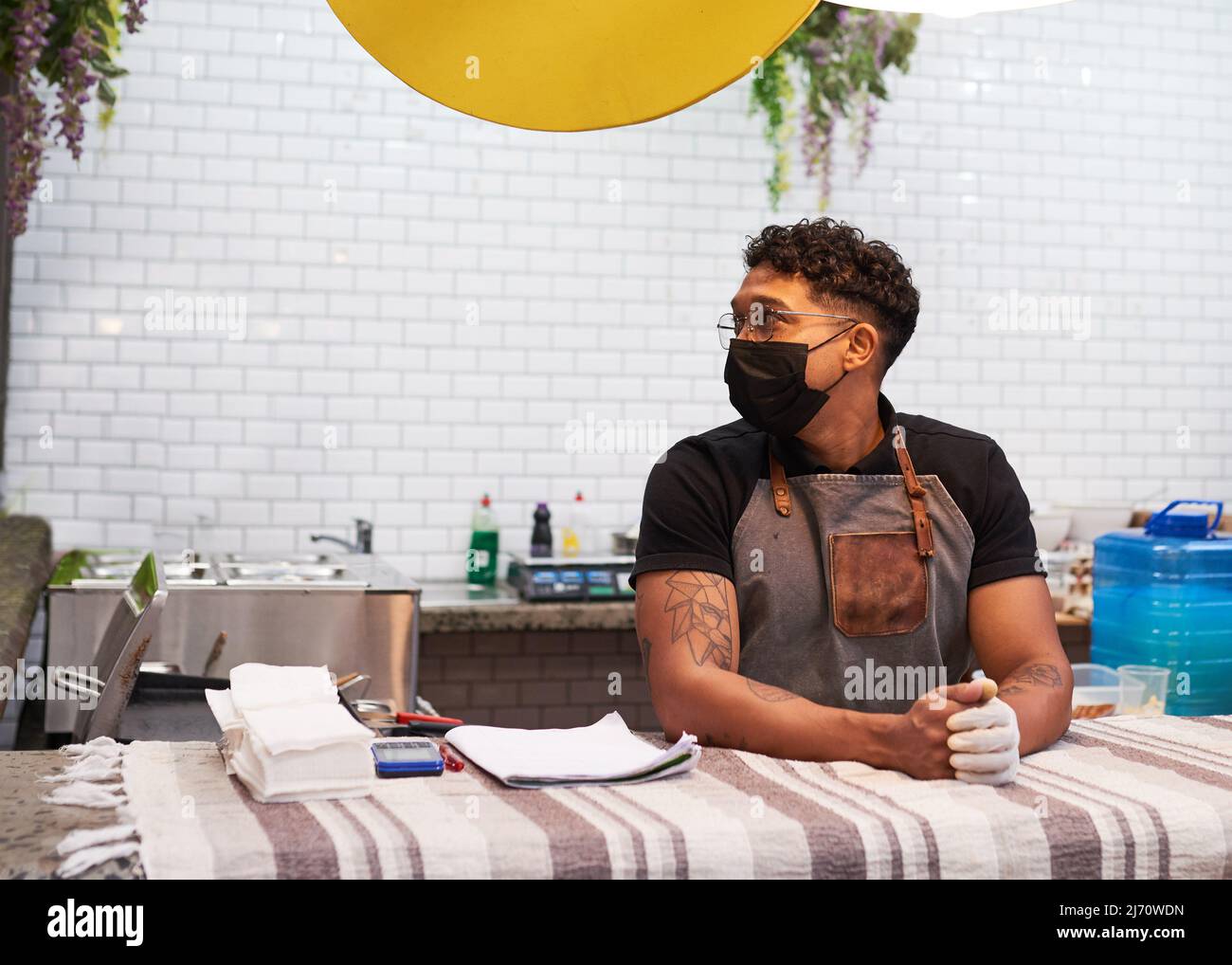 Un proprietario di piccola impresa si trova alla sua stalla di cibo in attesa di clienti con maschera Foto Stock