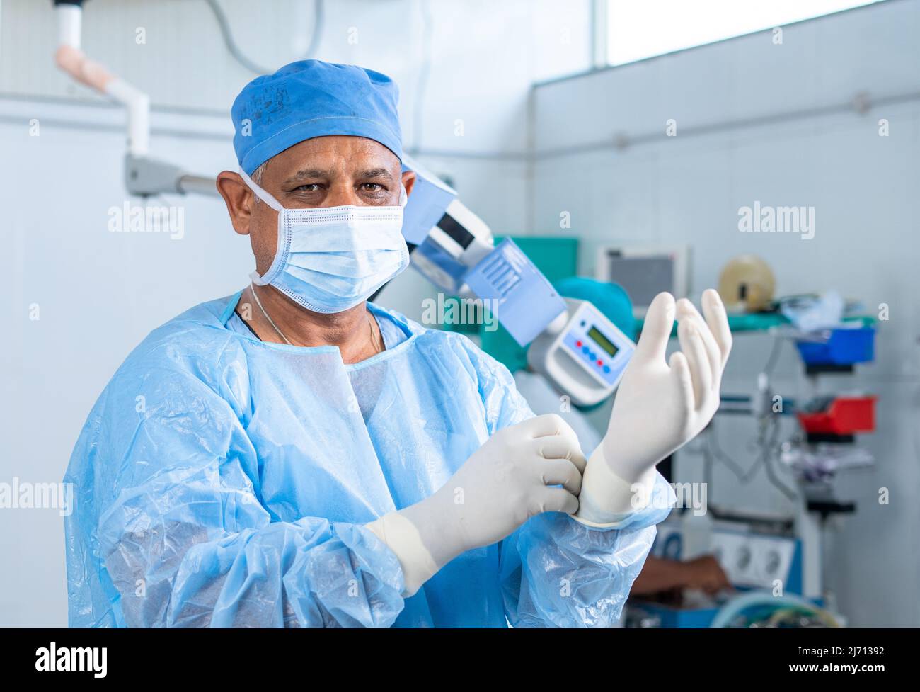 Chirurgo waring guanti per eseguire chirurgia in sala operatoria guardando fotocamera - concetto di preparazione, fiducia e medico profesionale Foto Stock