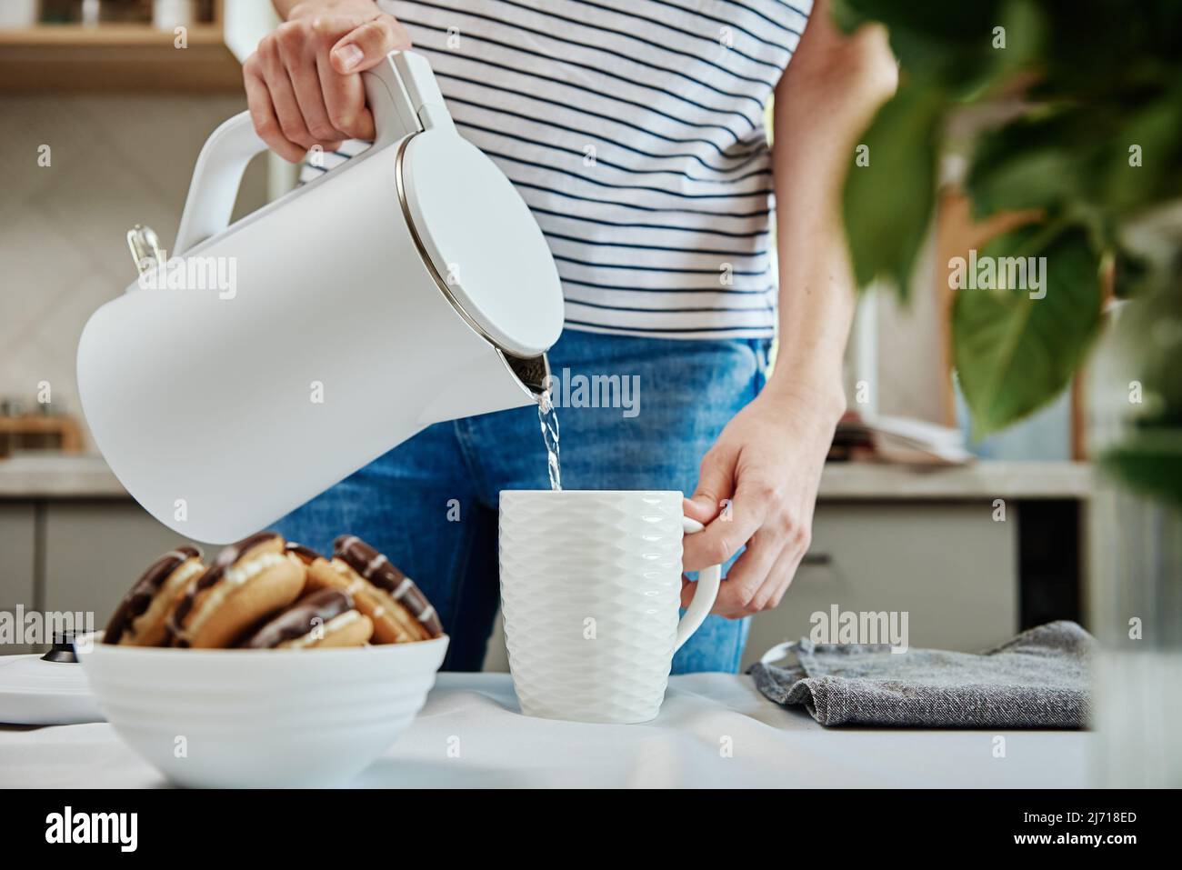 Tempo del tè, Donna versare acqua bollita dal bollitore elettrico in una tazza per preparare il tè, la prima colazione del mattino in cucina Foto Stock